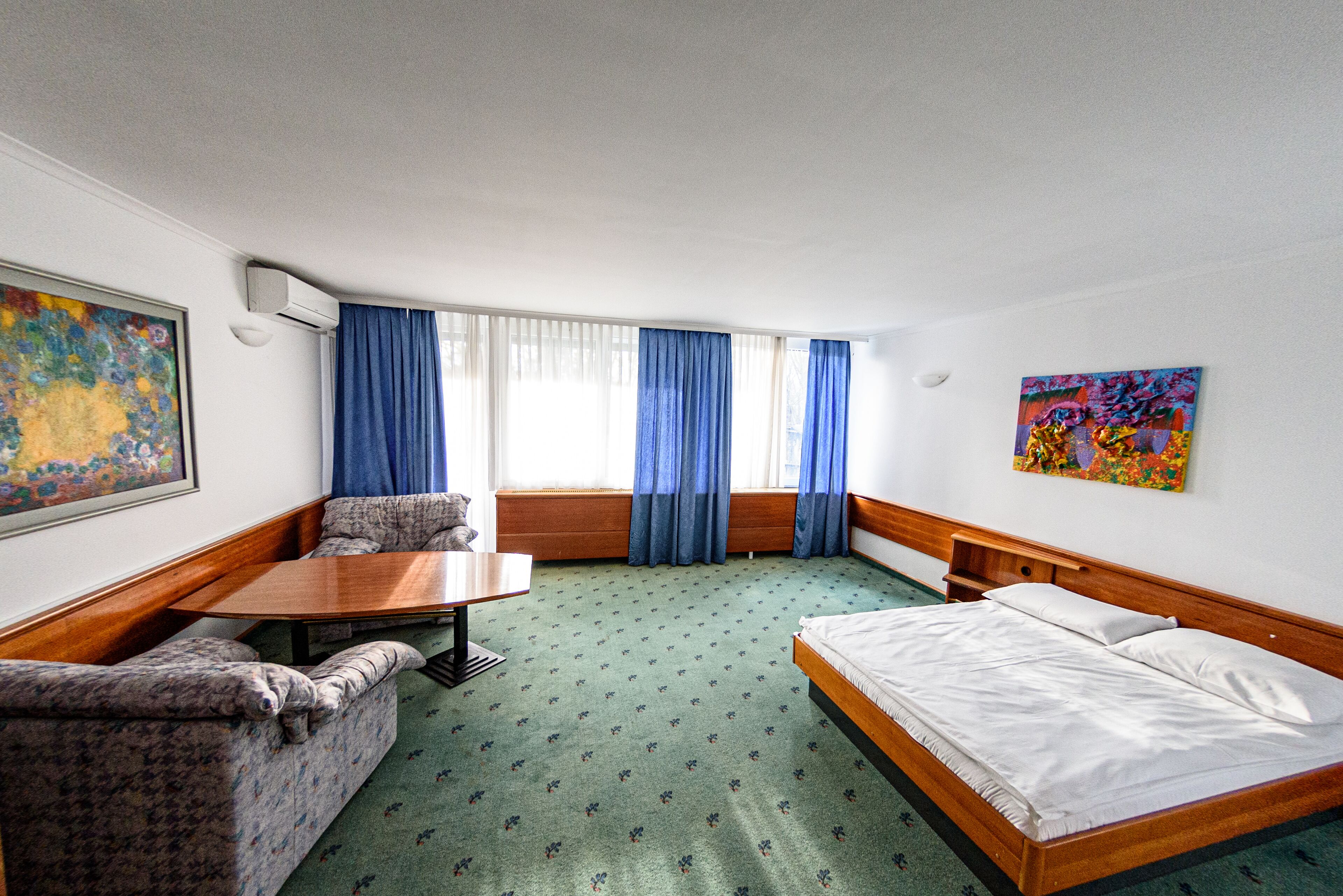 Habitación de hotel con cama, sofá, mesa y ventana con cortinas.