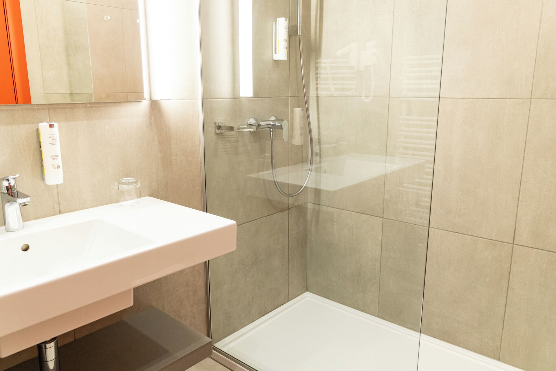 A bathroom with a white sink, a glass shower enclosure, and beige tiles.