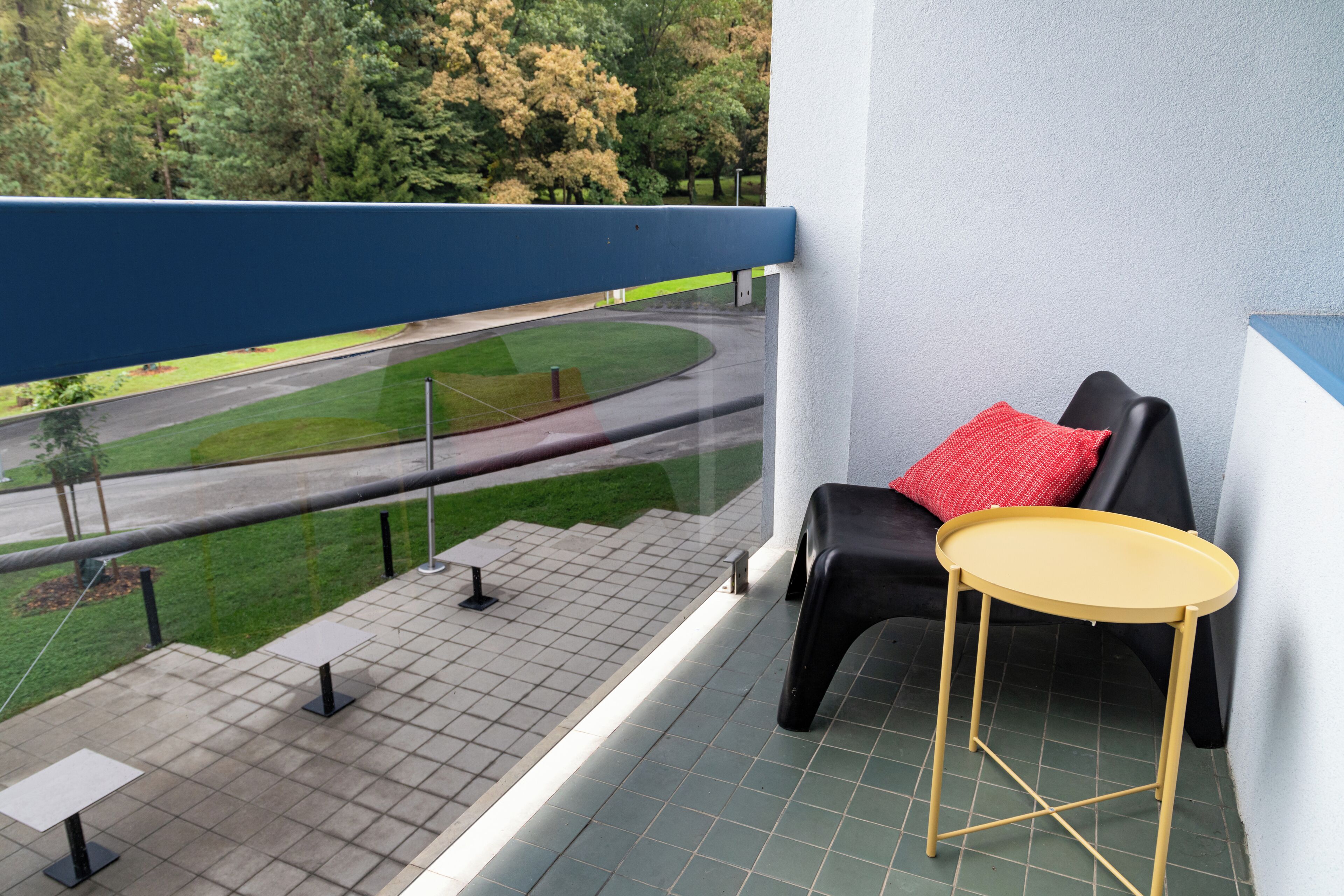 A balcony with a black sofa, a small round table, and a red pillow.