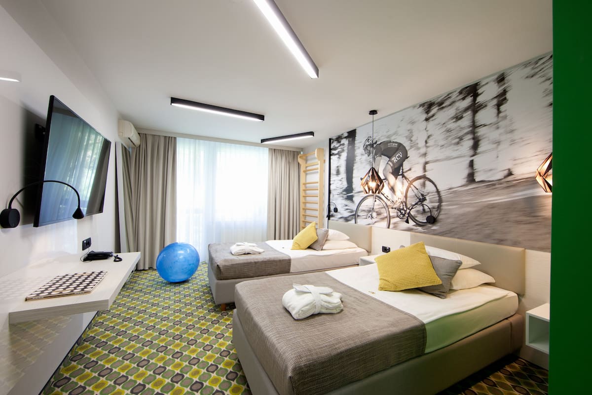 A hotel room with a TV, exercise ball, two beds, a desk, and a bicycle-themed wall art.