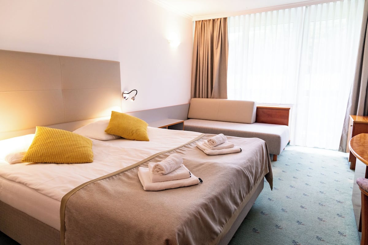 A hotel room with a large bed, two smaller beds, a sofa, and a desk.
