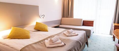 A hotel room with a large bed, two smaller beds, a sofa, and a desk.