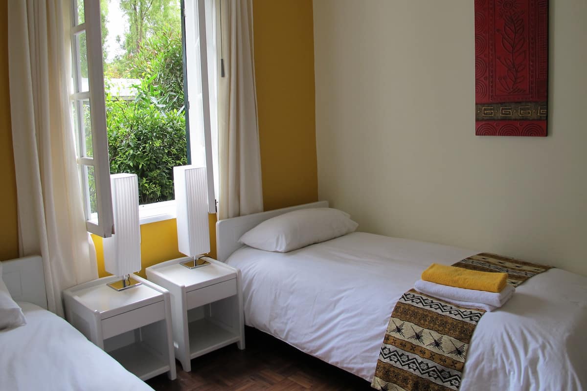 A room with two single beds, a window with curtains, a radiator, and a wall-mounted artwork.