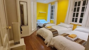 Quarto de hotel com duas camas, soalho de madeira, uma porta branca e um espelho.