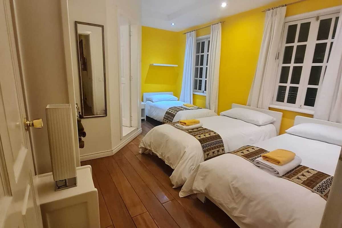 A hotel room with two beds, wooden flooring, a white door, and a mirror.