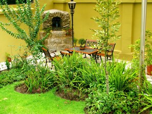 A patio with a stone oven, wooden table and chairs, and lush greenery. - Hotel Cayman (Quito)