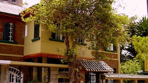 Um edifício com fachada amarela, uma árvore em frente e um portão com o sinal 'H' vermelho.