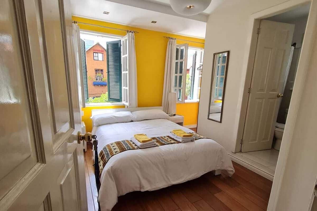 A bedroom with a bed, wooden flooring, a window with curtains, and a door.