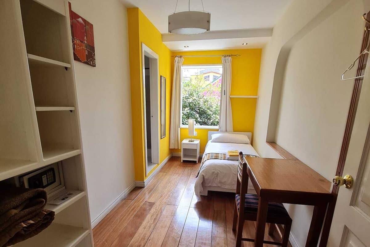 A bedroom with a bed, a wooden table, a wardrobe, and a window with curtains.
