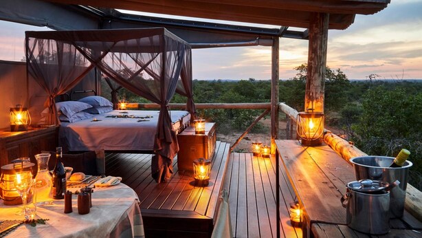 A cozy outdoor bedroom with a canopy bed, wooden deck, and lanterns providing ambient lighting. - Motswari Private Game Reserve Resort by NEWMARK (Bushbuckridge)