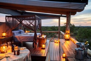 A cozy outdoor bedroom with a canopy bed, wooden deck, and lanterns providing ambient lighting. - Motswari Private Game Reserve Resort by NEWMARK (Bushbuckridge)