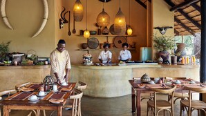 A restaurant with a central counter, wooden tables, and chairs. There are hanging lights and decorative items on the walls. - Motswari Private Game Reserve Resort by NEWMARK (Bushbuckridge)