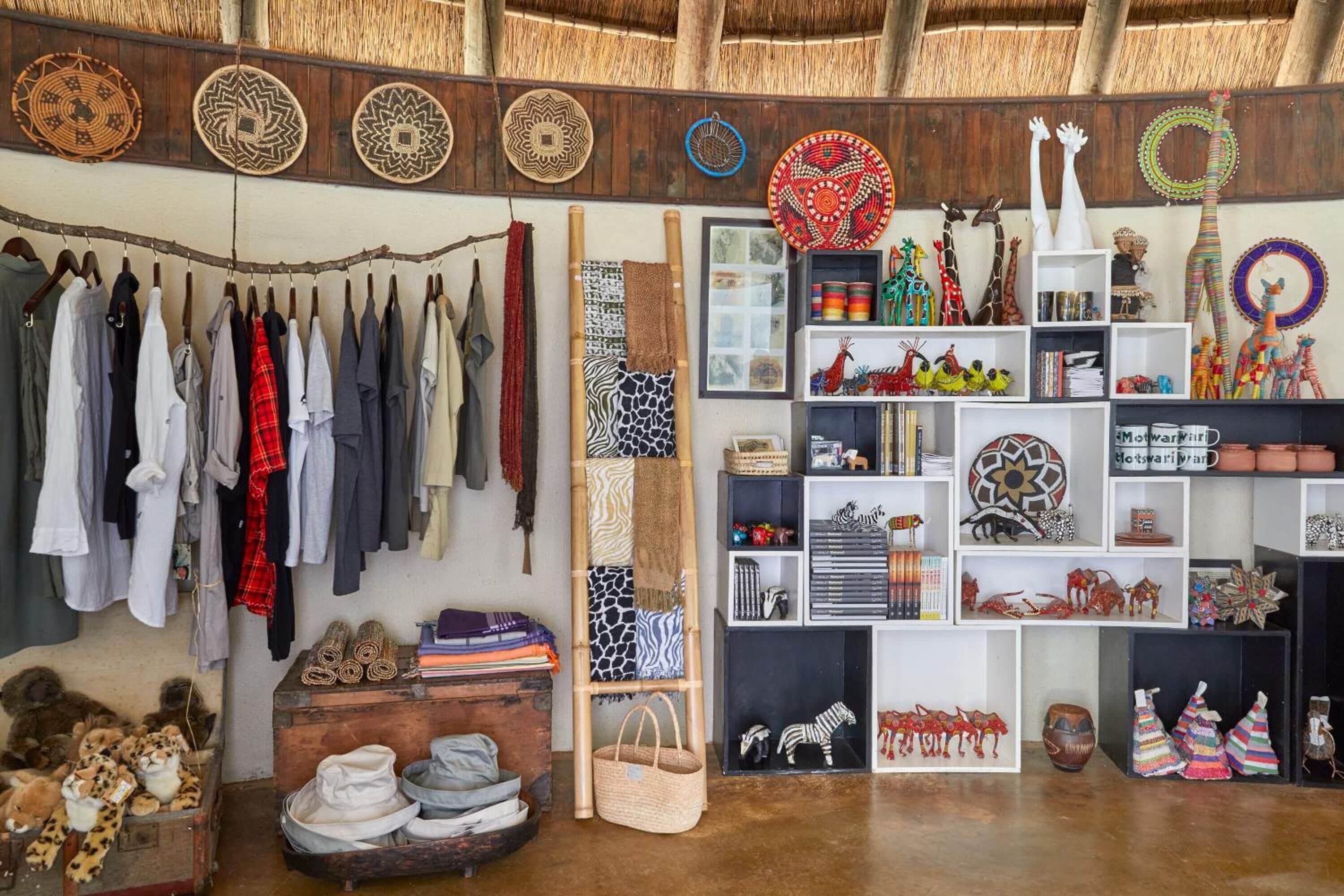 A room with a rustic ceiling, a clothing rack with various garments, shelves with decorative items, and a wooden chest with patterned textiles.
