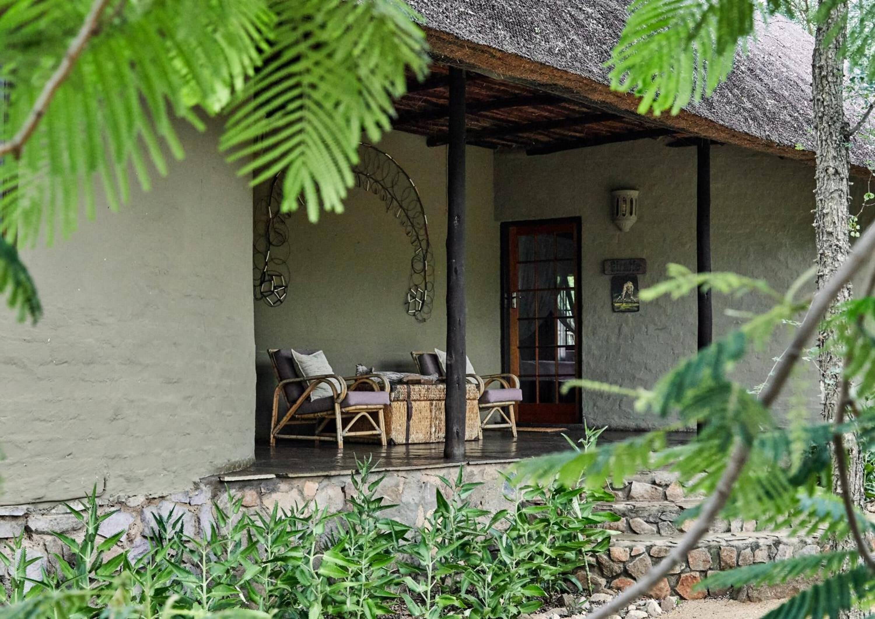 A rustic building with a thatched roof, a porch with wicker furniture, and a stone wall.