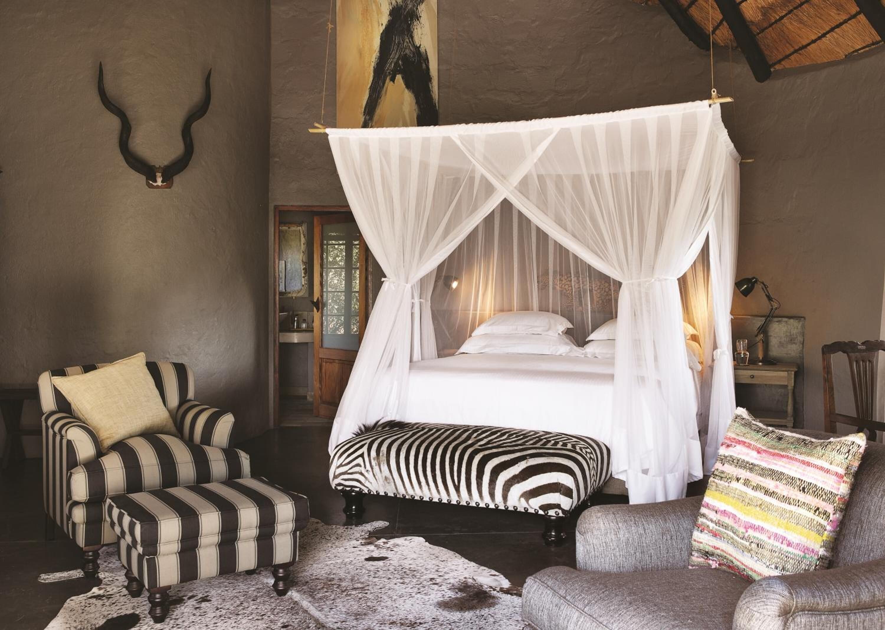 Un dormitorio con cama de dos plazas, sillones a rayas y un reposapiés estampado con diseño de cebra.
