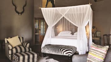 A bedroom with a four-poster bed, striped armchairs, and a zebra-patterned ottoman.