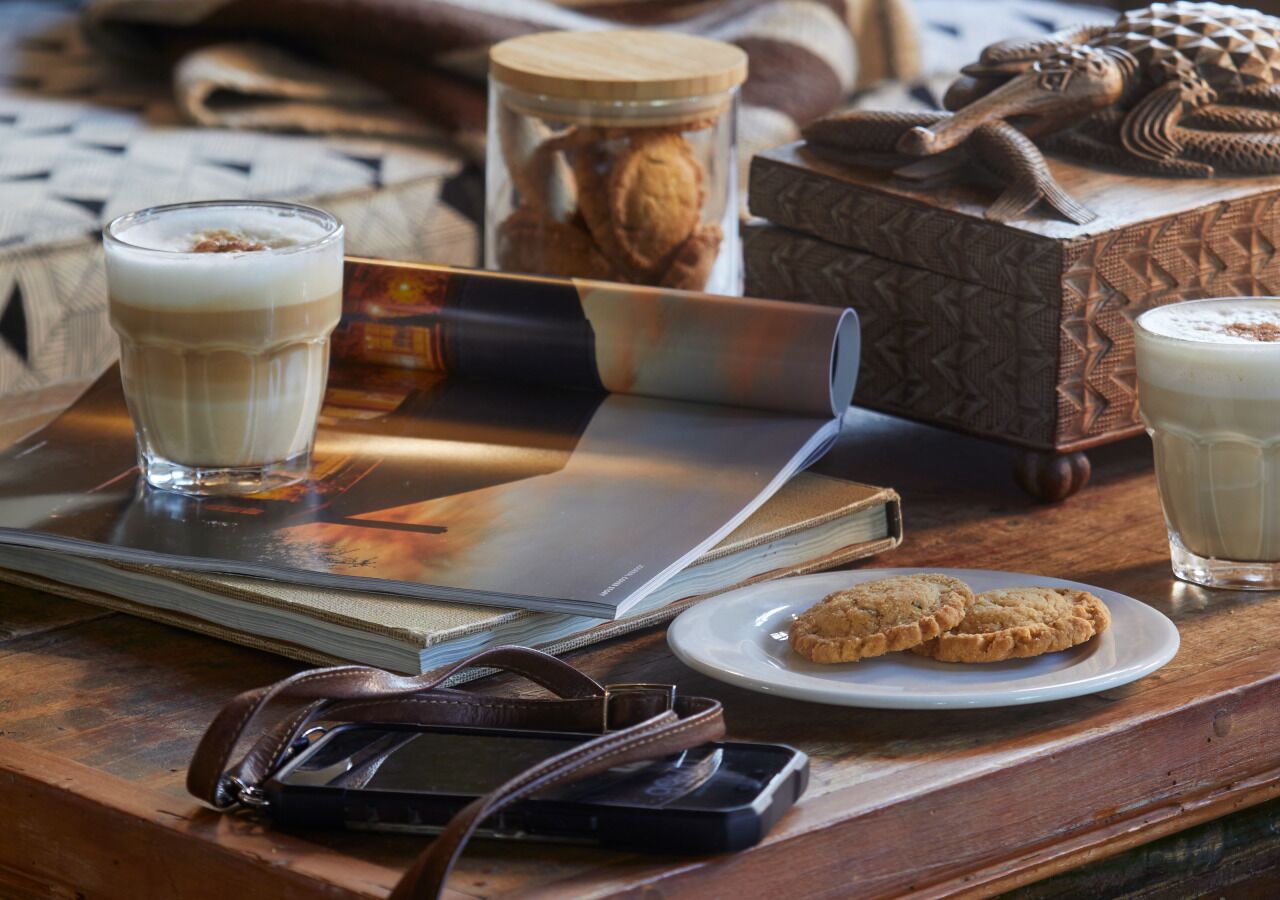 A wooden table with a book, a glass of milk, a plate of cookies, a jar of cookies, and a smartphone.