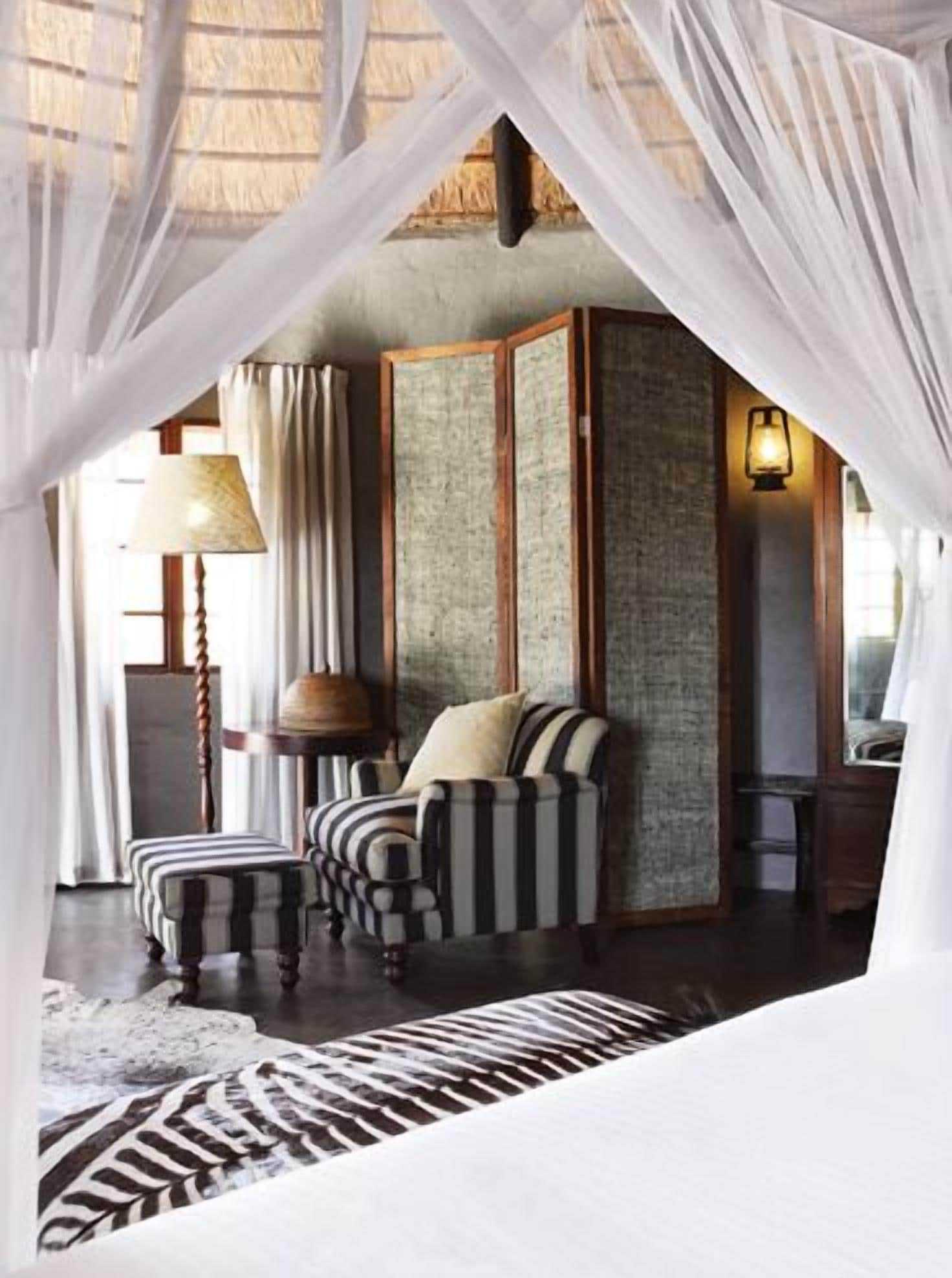 A room with a bed, striped armchairs, a lamp, and a textured wall.
