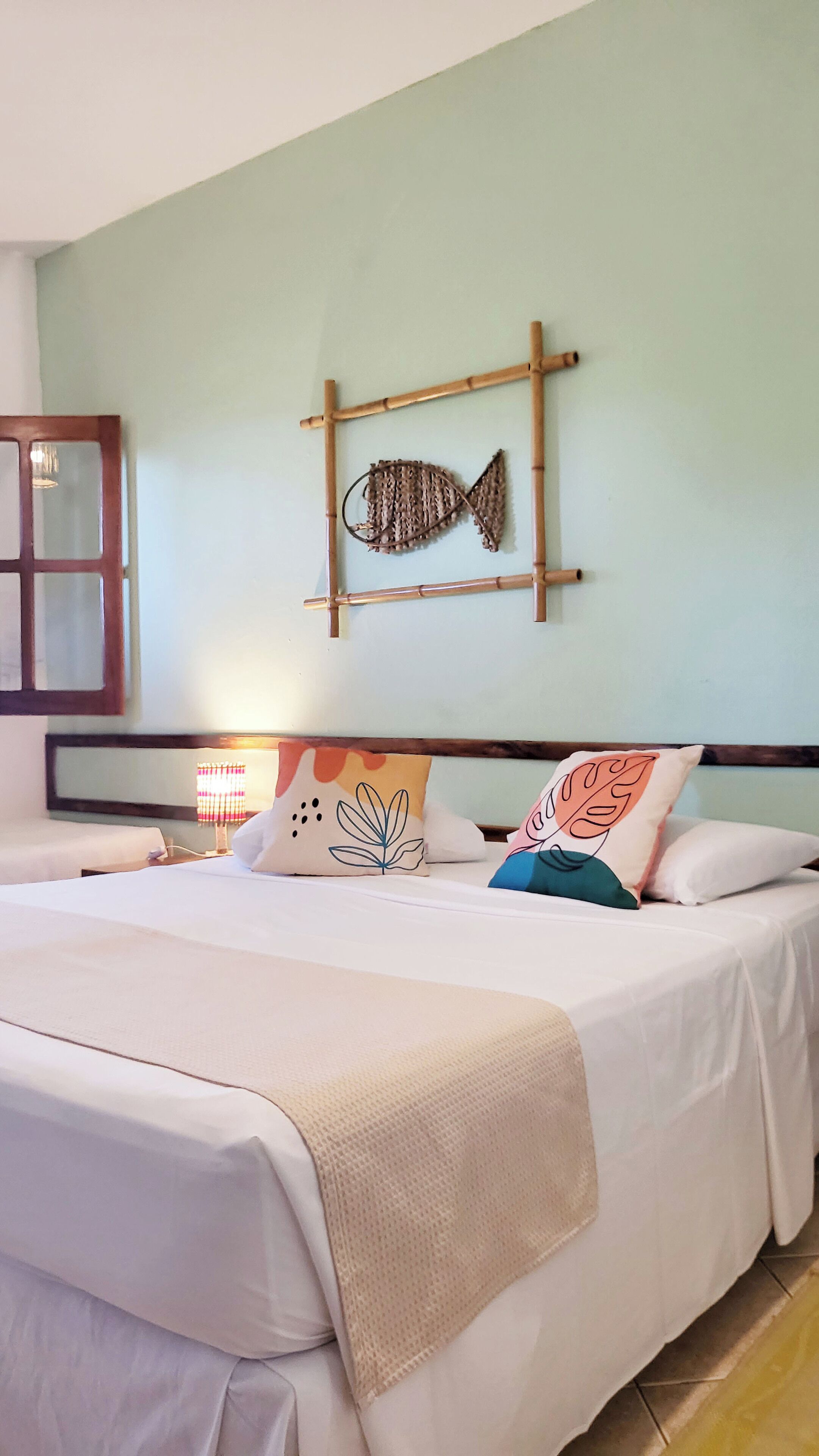 A hotel room with a bed, a wall-mounted fish decoration, and a window with curtains.