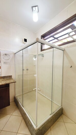 A glass-enclosed shower stall with a tiled floor and a wooden countertop to the left.