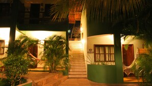Um edifício com escadaria que leva a um segundo andar, cercado por plantas em vasos e uma estrutura de telhado de palha.
