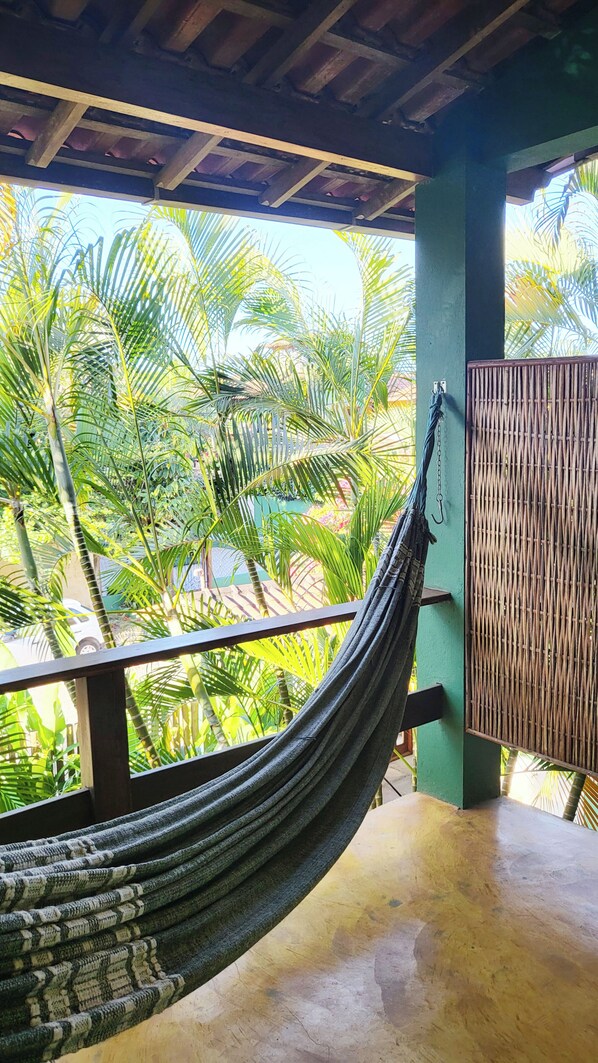 A hammock hanging on a balcony with a view of palm trees and a pool.