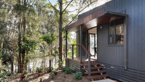 Una casa moderna con terraza de madera, una escalera y vistas a un área boscosa.