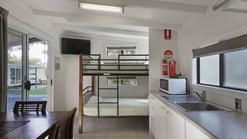 Een slaapkamer met stapelbedden, een keukenhoek met een magnetron, spoelbak en kastjes, en een eettafel met stoelen.