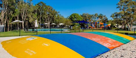Zona de playa con un espacio de juego en la arena lleno de color, sombrillas y un parque infantil vallado.