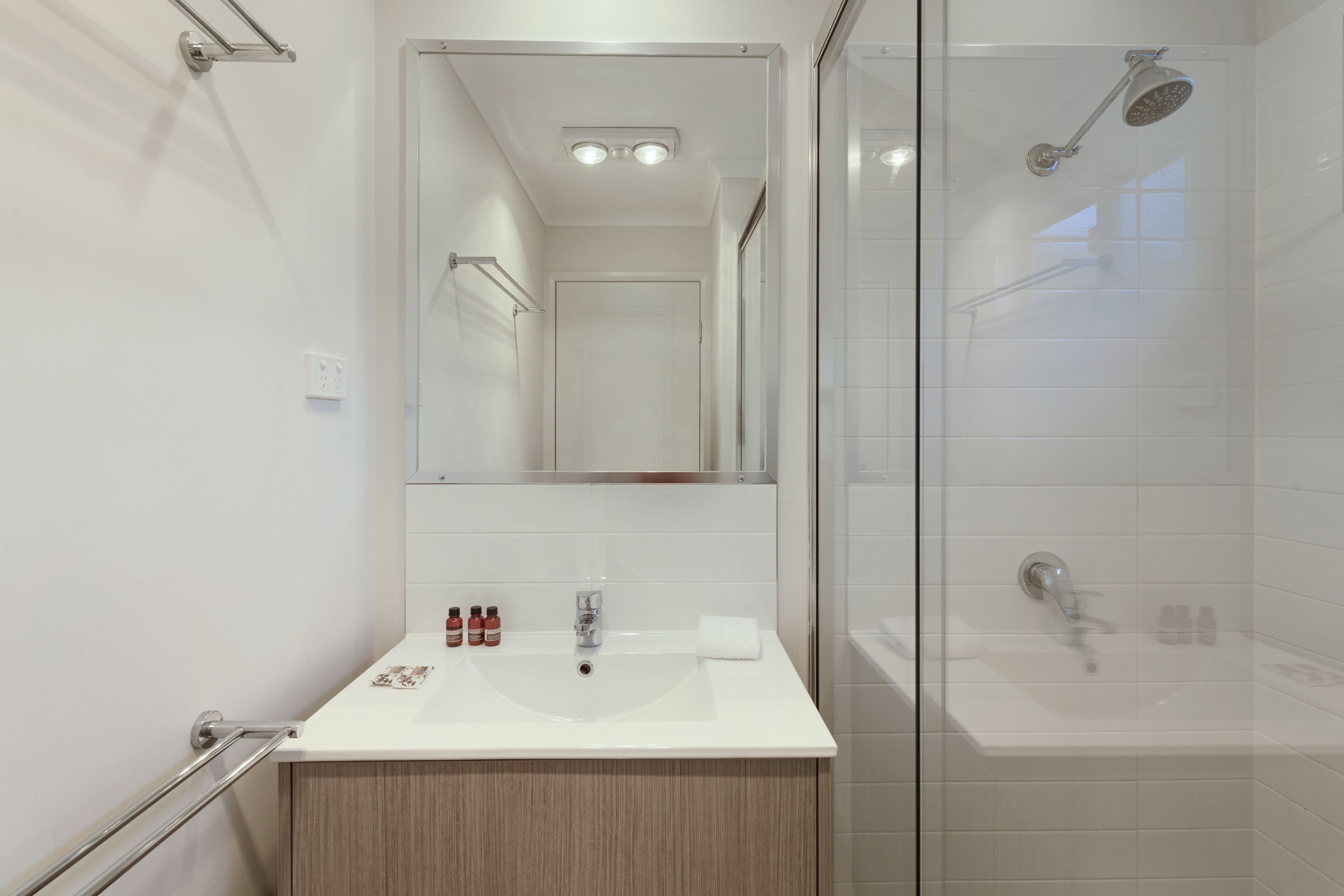 A modern bathroom with a glass-enclosed shower, a white sink with a mirror above it, and a wooden cabinet below.