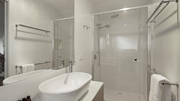 Un baño moderno con un lavabo grande de color blanco, una ducha con mampara de vidrio y un espejo sobre el lavabo.