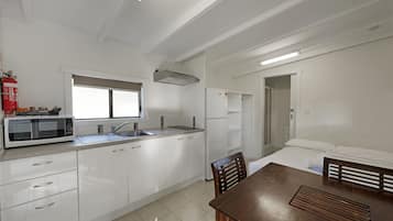 Una cocina moderna con armarios blancos, un microondas y un fregadero. Hay un comedor con una mesa y sillas de madera.