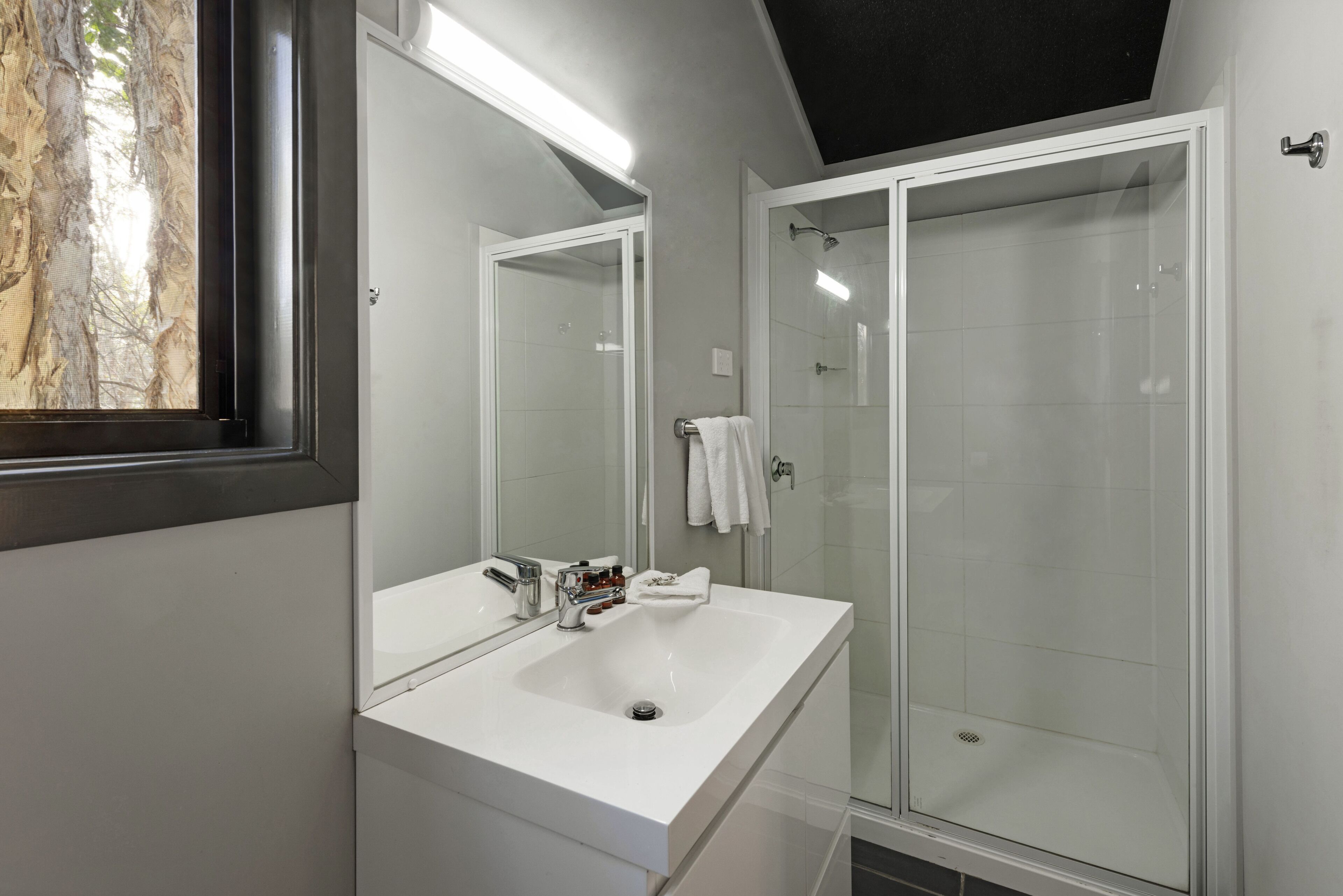 Un baño moderno con un espejo grande, un lavabo blanco y una ducha con mampara de vidrio.