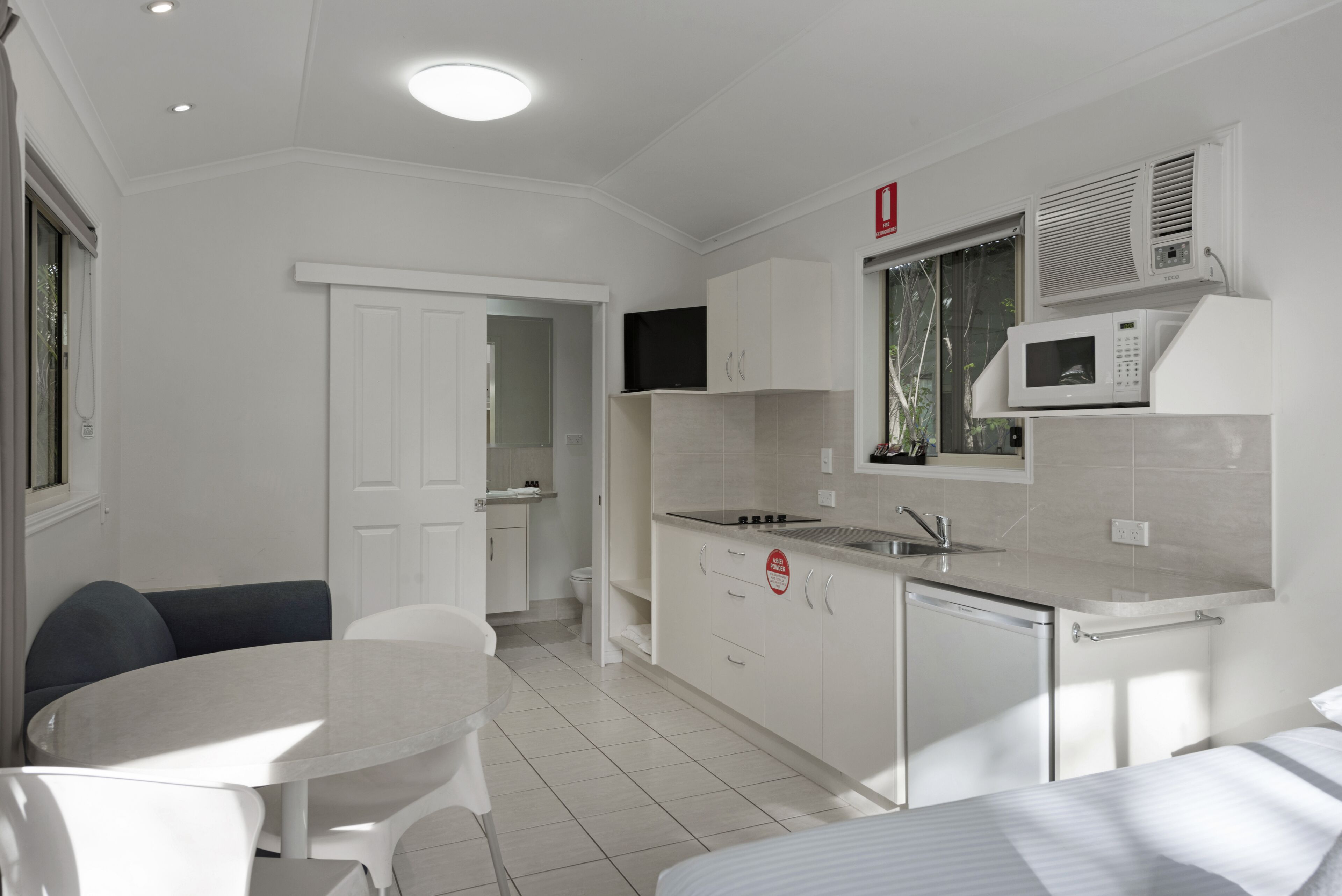 A compact kitchen with white cabinetry, a microwave, and a sink. There is a dining area with a table and chairs.