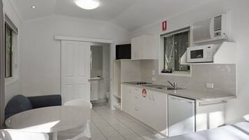 A compact kitchen with white cabinetry, a microwave, and a sink. There is a dining area with a table and chairs.