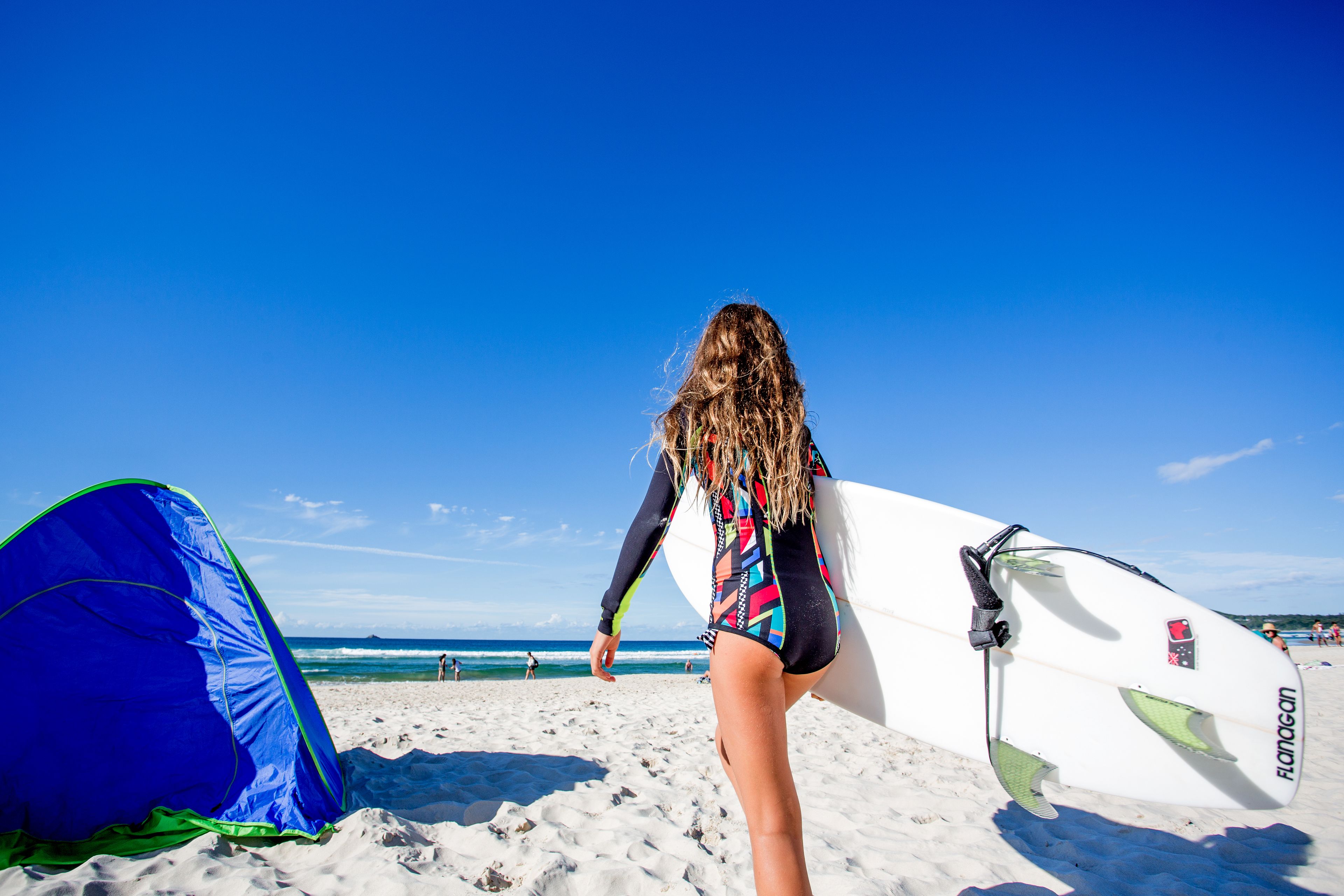 Escena de playa con una tienda de campaña y una tabla de surf.