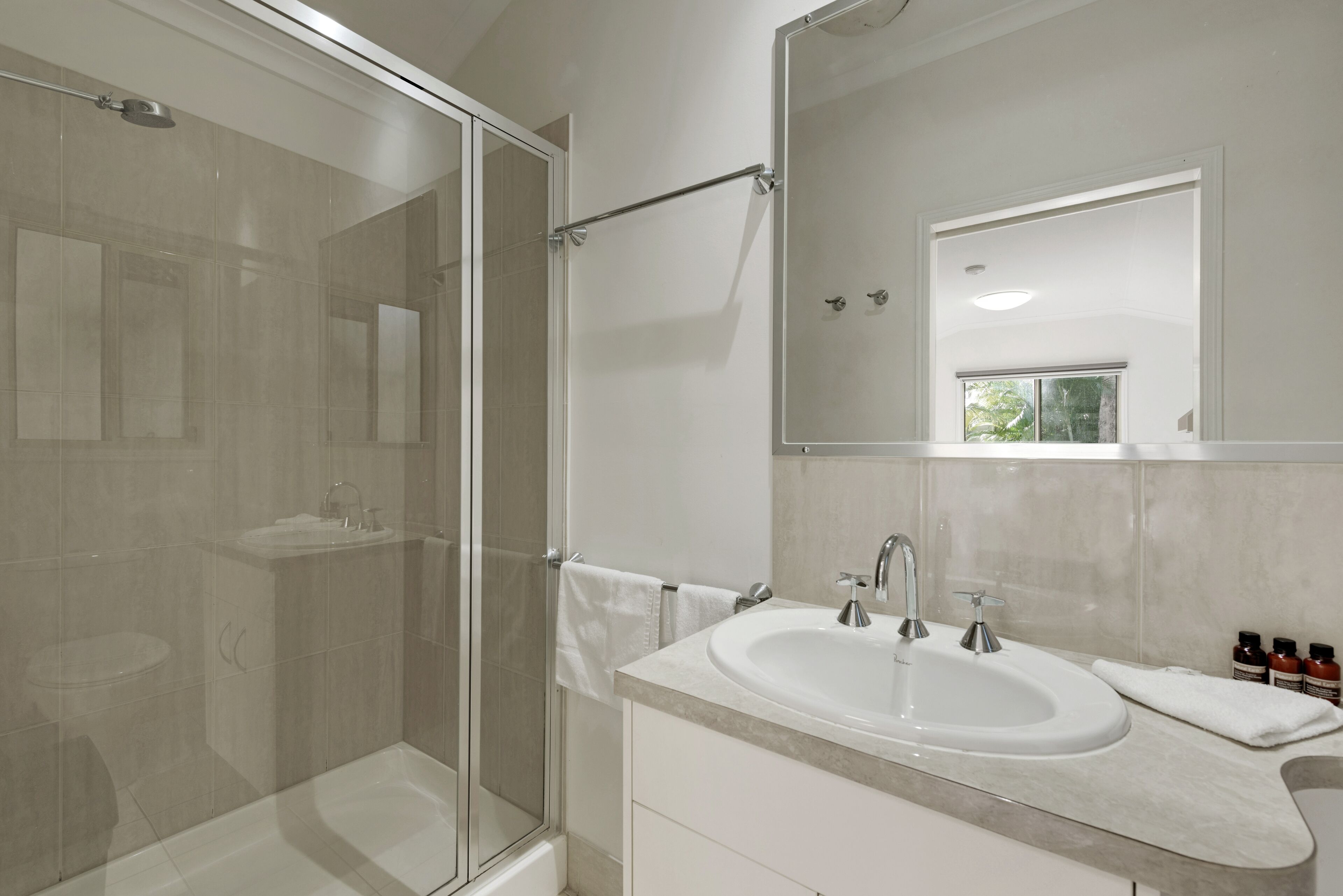 A modern bathroom with a glass shower enclosure, a sink with a mirror, and a window.