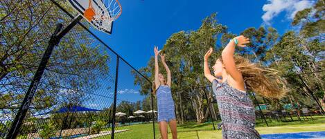 An outdoor basketball court with a net, a basketball hoop, and trees in the background.
