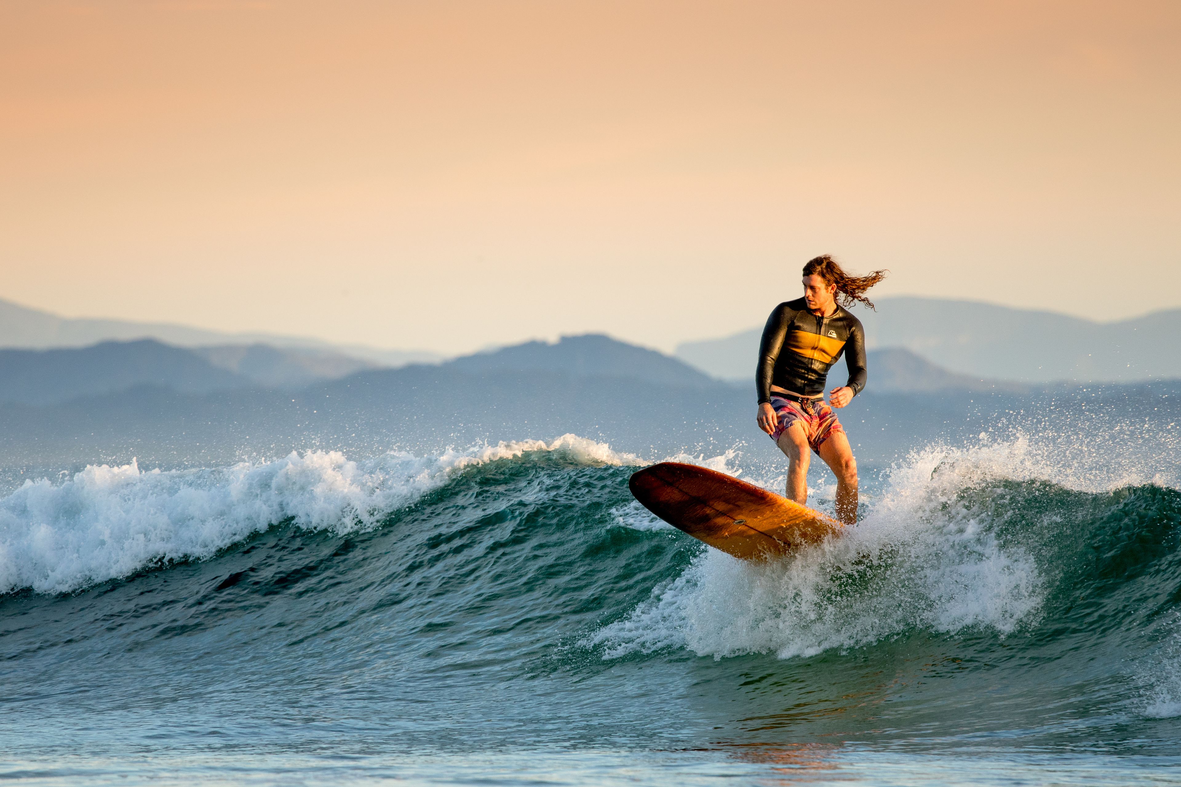 A surfer riding a wave with mountains in the background.