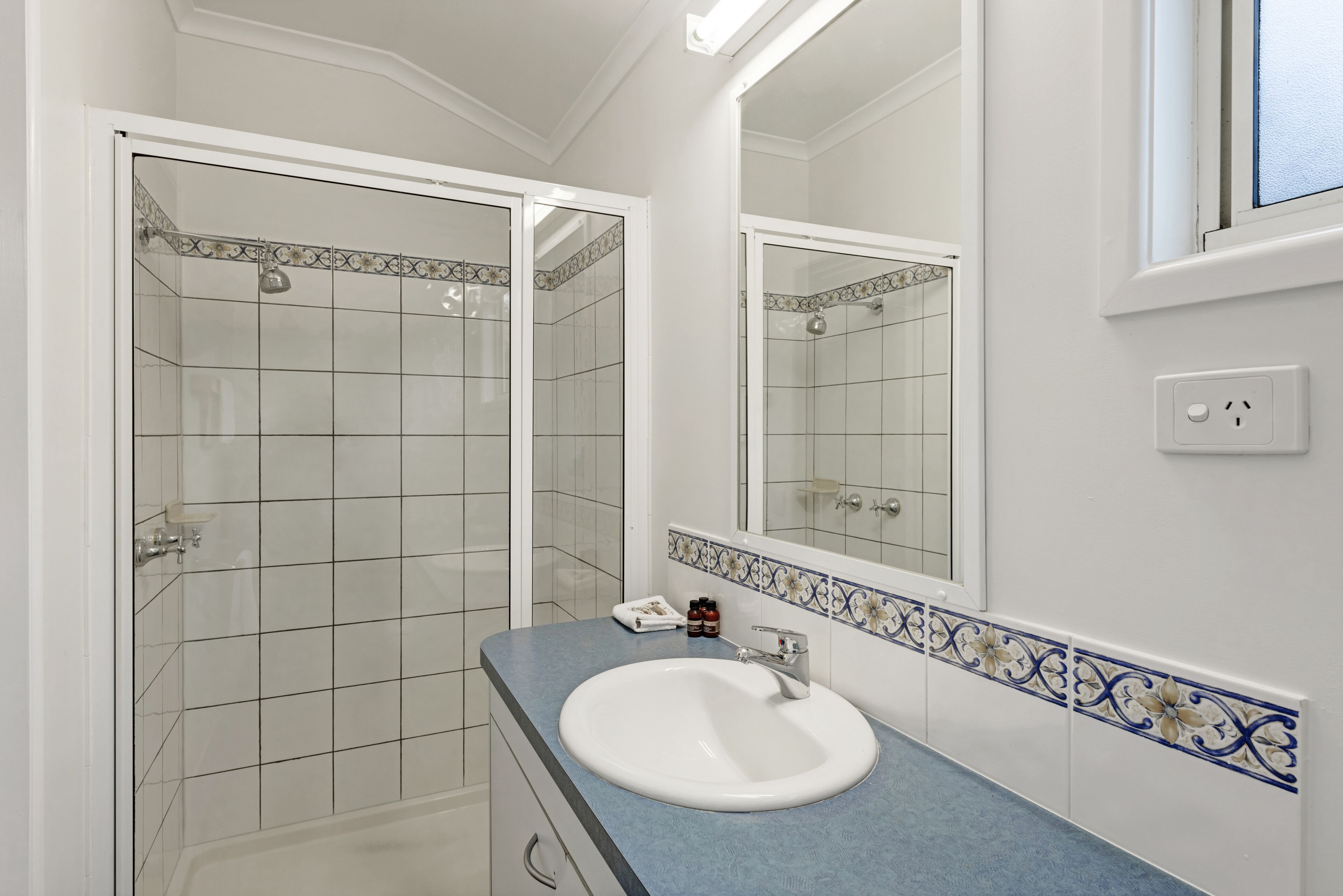 Een badkamer met een wit wastafel, een spiegel en een douchecabine.