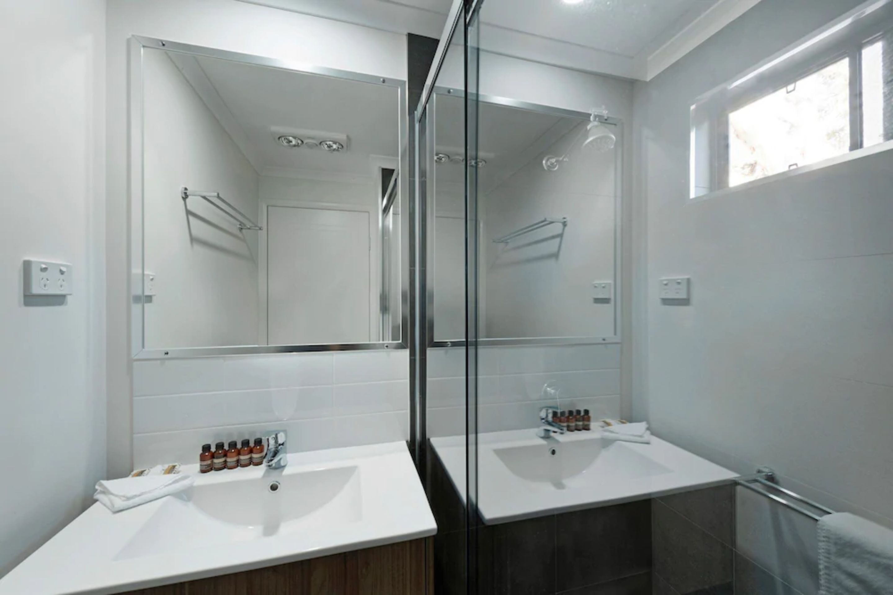 Une salle de bain moderne avec deux lavabos, un grand miroir et une douche à l’italienne.