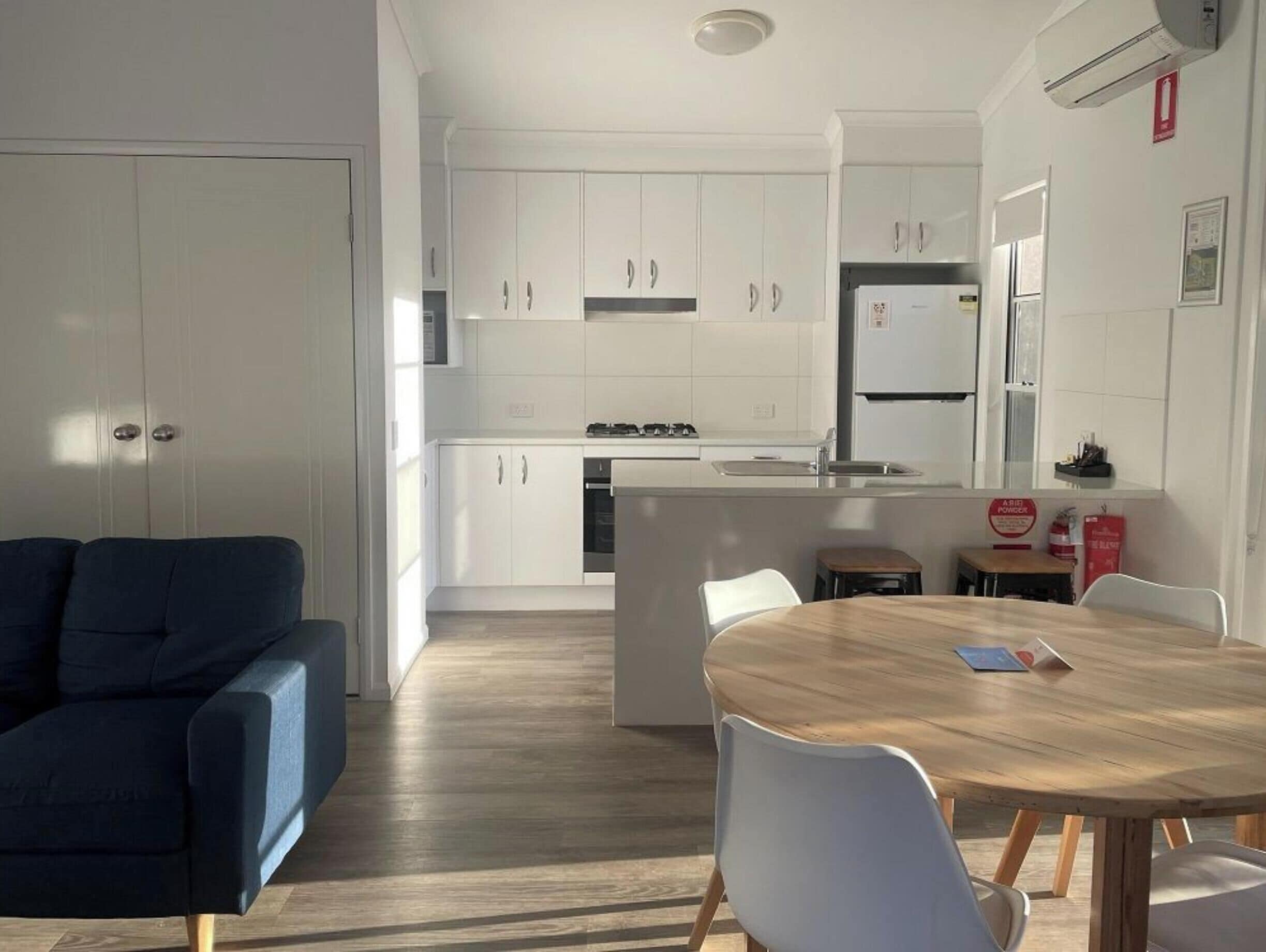 Una cucina moderna con mobili bianchi, un'isola centrale e un'area pranzo con tavolo in legno e sedie bianche.