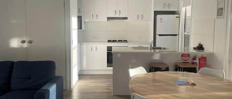 Una cucina moderna con mobili bianchi, un'isola centrale e un'area pranzo con tavolo in legno e sedie bianche.