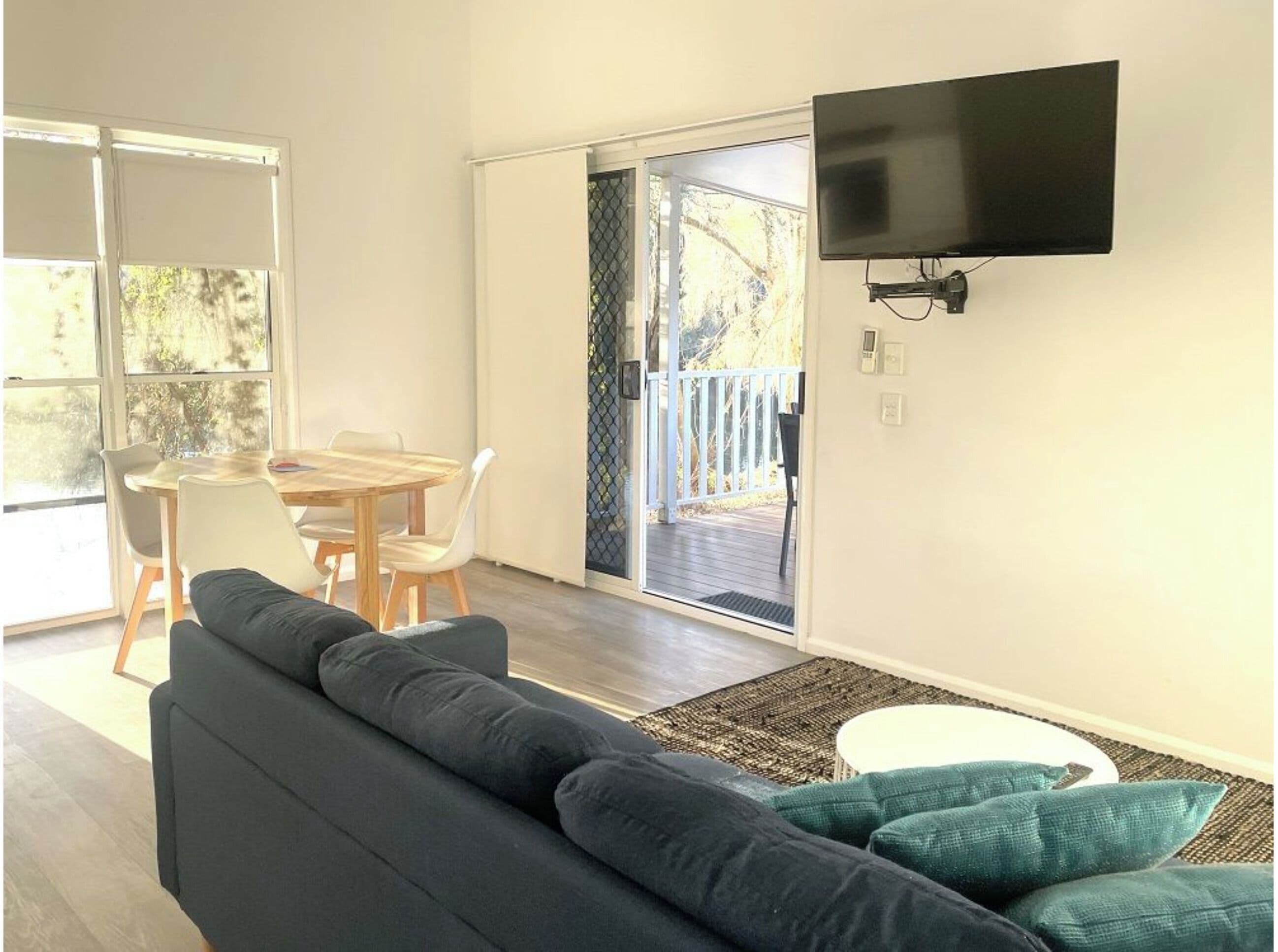 A living room with a dark sofa, a small round table, and a TV mounted on the wall.