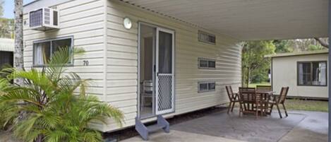 A mobile home with a covered patio, a small table and chairs, and a palm tree.