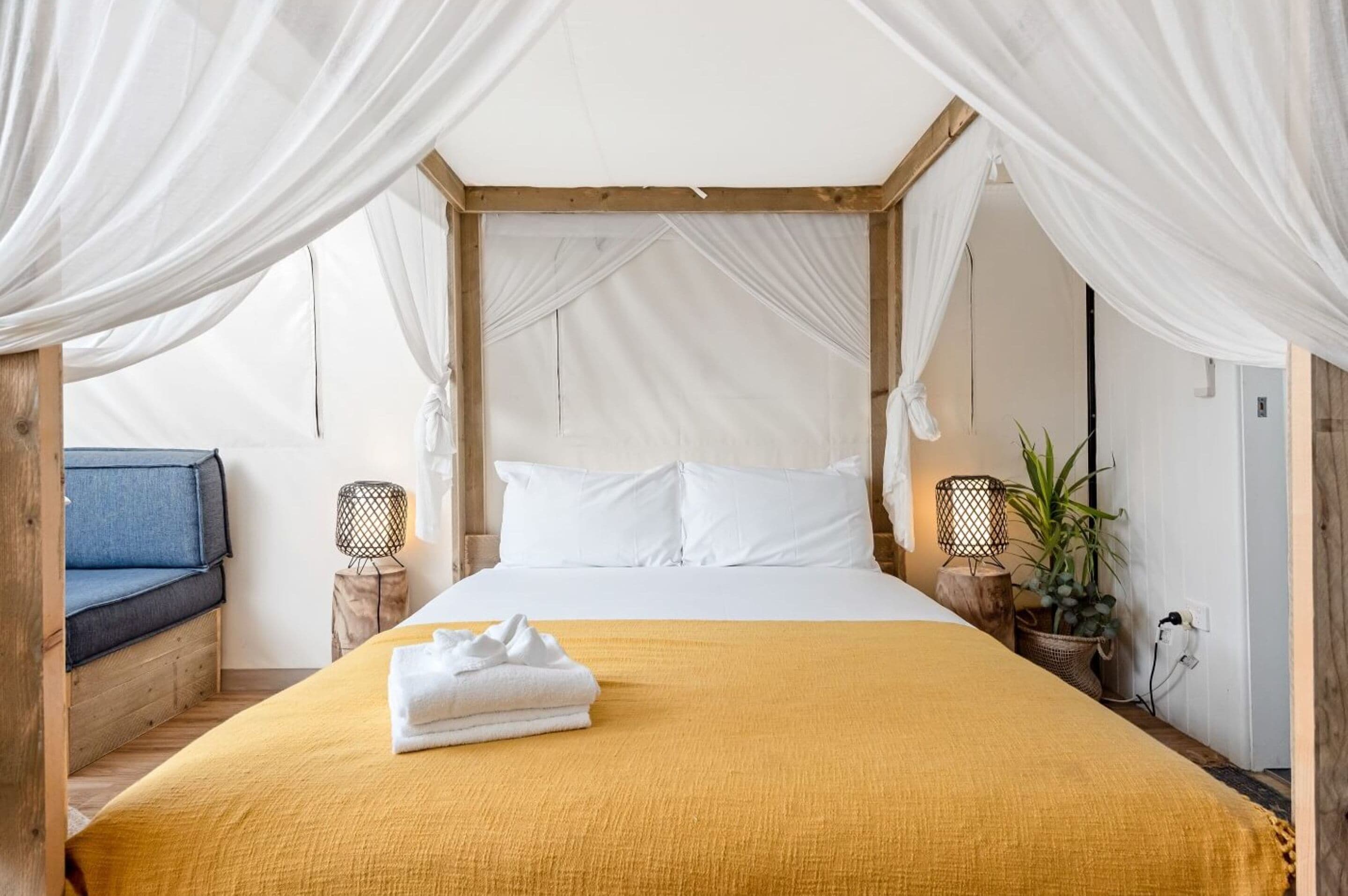 A bed with a canopy, white bedding, and a yellow throw blanket.