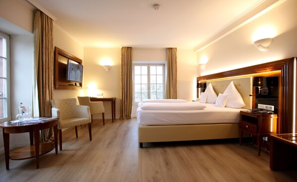 A hotel room with a large bed, two bedside tables, a desk with a chair, a television on the wall, and a window with curtains.