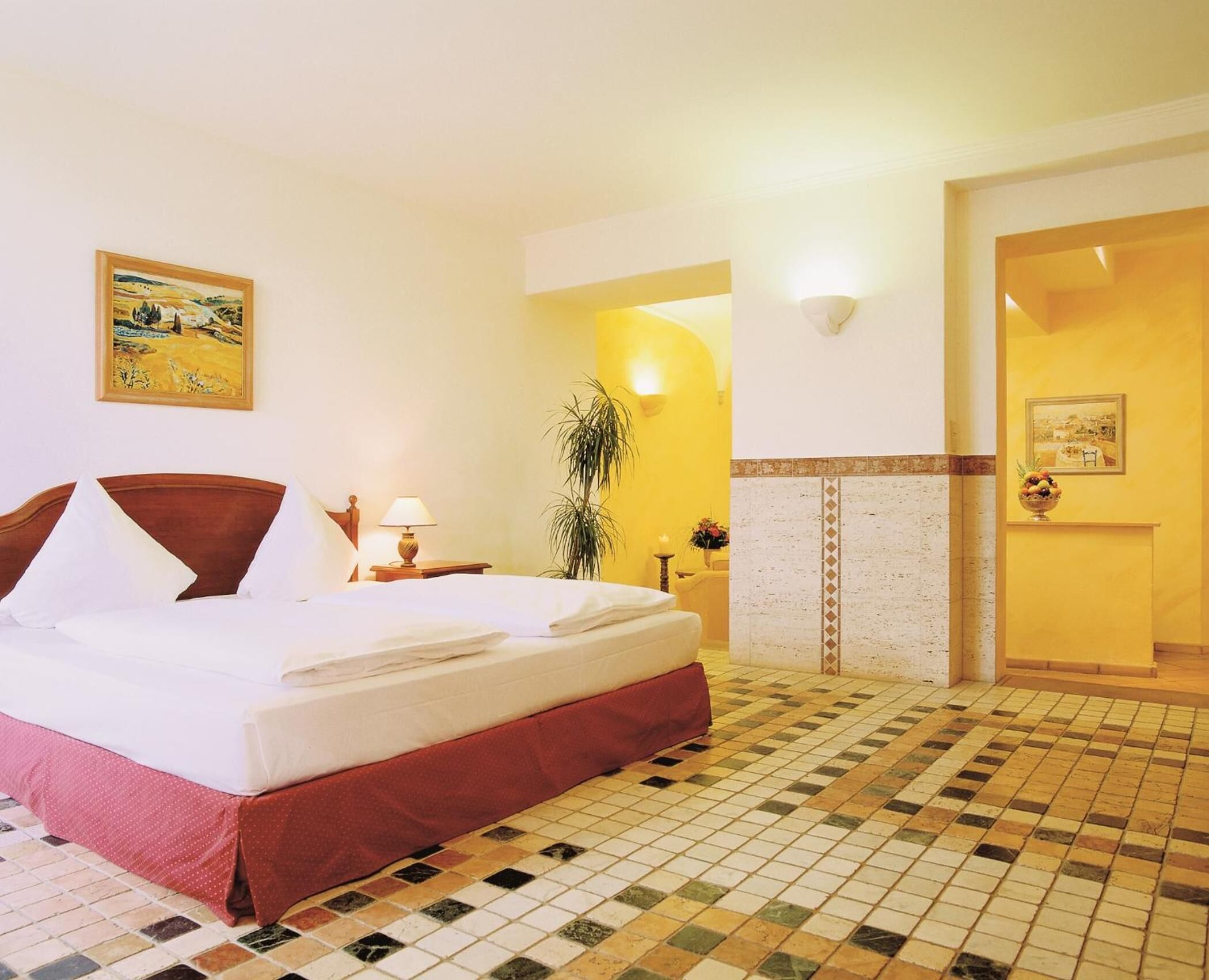Une chambre d’hôtel avec un grand lit, une table de chevet, une lampe, un tableau au mur et un sol carrelé.