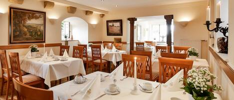 A dining area with tables set for service, wooden chairs, and a chandelier.