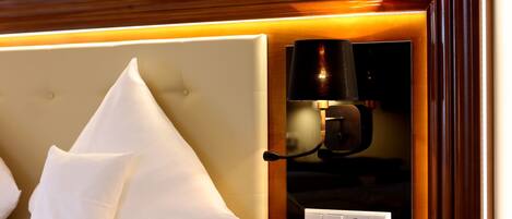 Une chambre d’hôtel avec un lit, des oreillers blancs, une table de chevet avec un téléphone et une lampe fixée au mur.